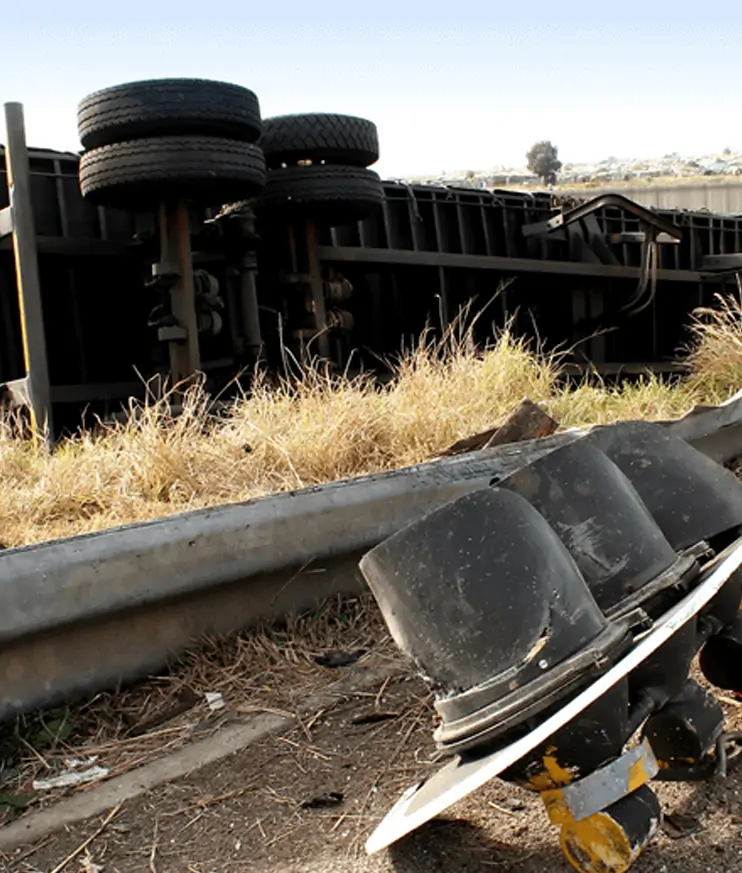 An overturned truck beside a damaged roadside guardrail